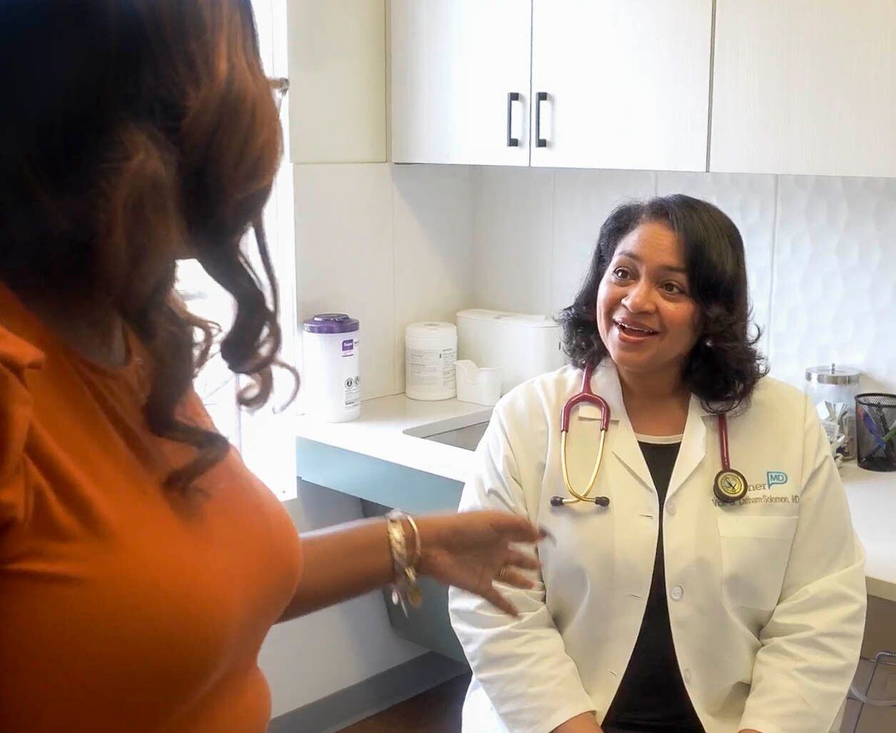 Dr. Vicki Latham-Solomon, a concierge doctor at PartnerMD Midlothian, talks to a patient while sitting down in an exam room