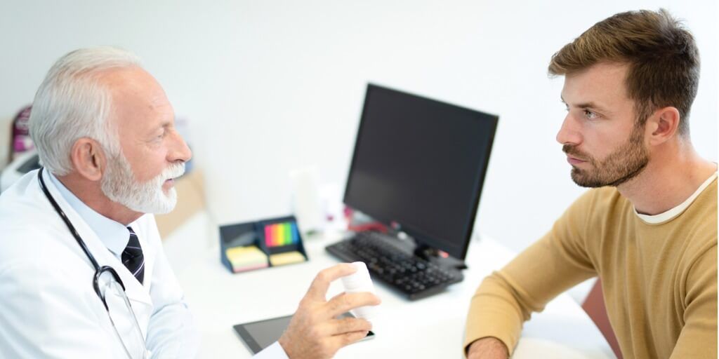 Older male physician talking with a patient at desk